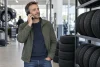 Un client téléphone dans un centre automobile neutre, près de pneus rangés.