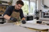 Un artisan protégé recolle à plat un tissu de pavillon démonté sur un établi ventilé.